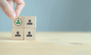 手がユーザーアイコンの描かれた木のブロックを選んでいる様子。ペルソナ作成における特定ユーザーの選定を表している。