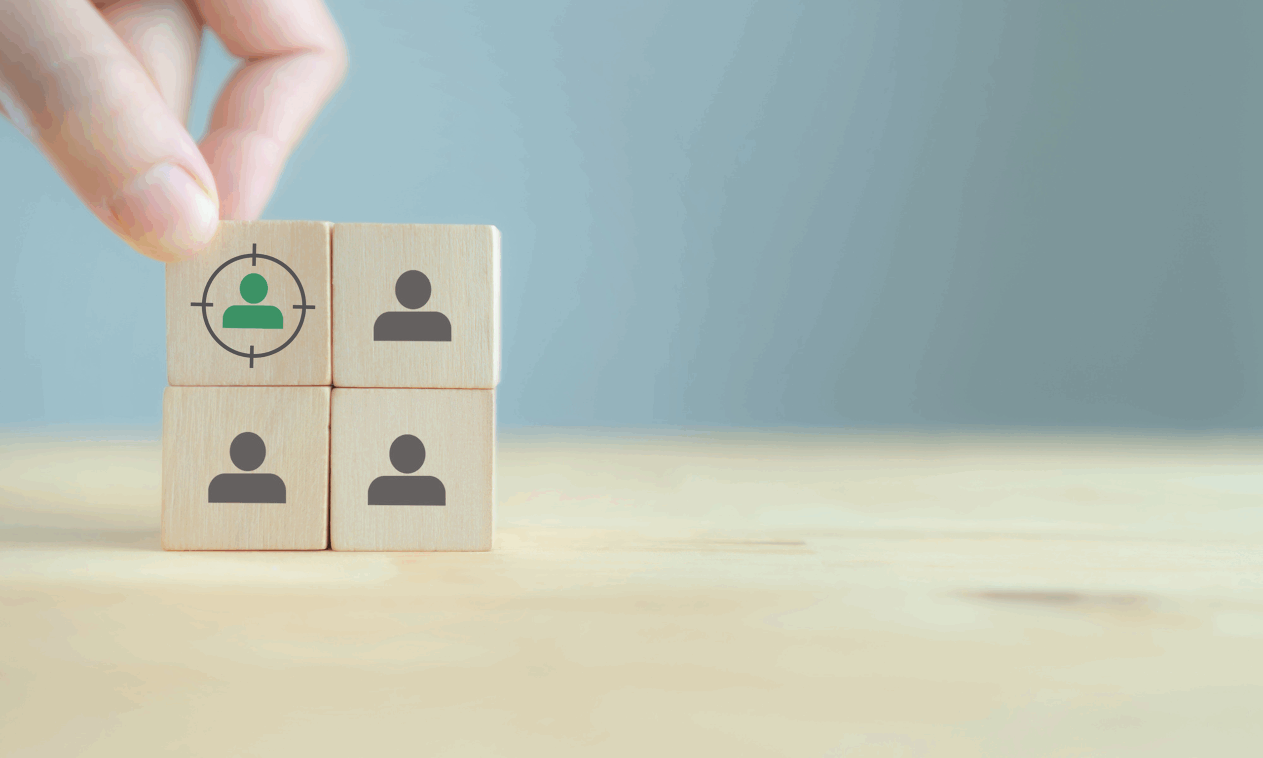 手がユーザーアイコンの描かれた木のブロックを選んでいる様子。ペルソナ作成における特定ユーザーの選定を表している。