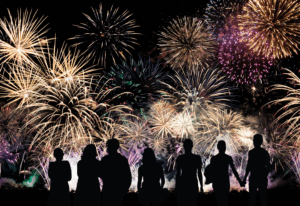 Japanese fireworks festival at night, with silhouettes of people watching colorful bursts over a river — a shared cultural UX experience of awe and reflection.