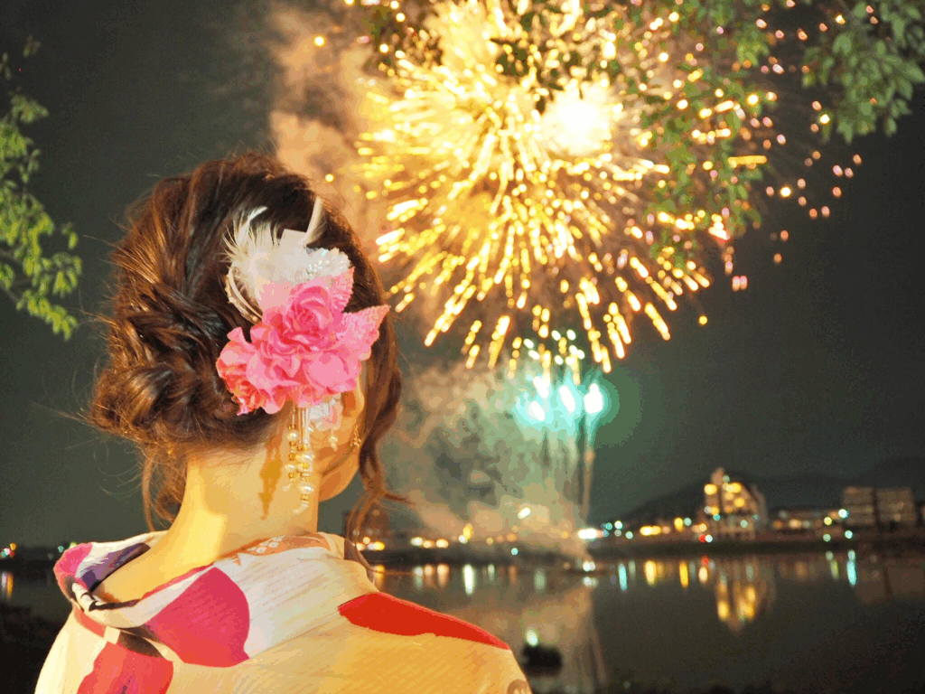 浴衣姿の女性が夏の夜空の花火を見上げるシーン。日本文化に根づいた情緒的な体験デザインの象徴。
