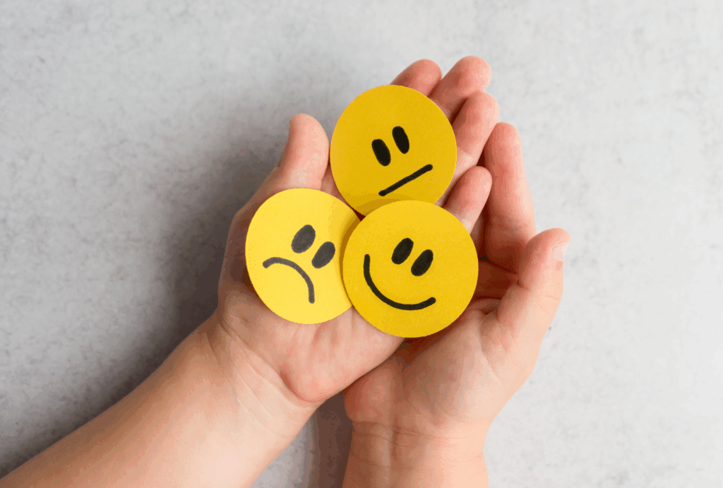 両手に乗せられた、笑顔・真顔・悲しい顔の3つの絵文字。日記調査が、ユーザーの日々の行動だけでなく、それに伴う感情の変化を時系列で捉えるUXリサーチ手法であることを象徴している。