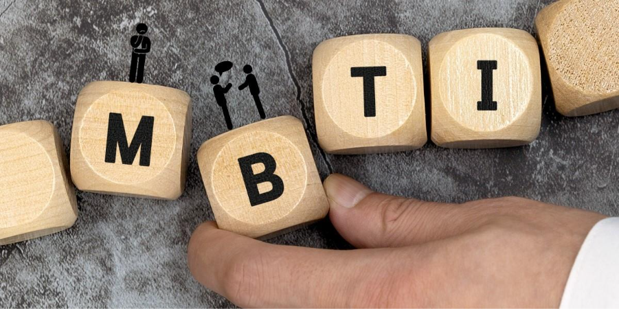 Wooden blocks spell out MBTI. A stick figure stands alone on the 'M' block, representing self-understanding, while two figures converse on the 'B' block, symbolizing making connections through MBTI.