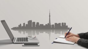 Laptop and notebook on a desk with a Tokyo skyline silhouette in the background, representing UX research and fieldwork in Japan.
