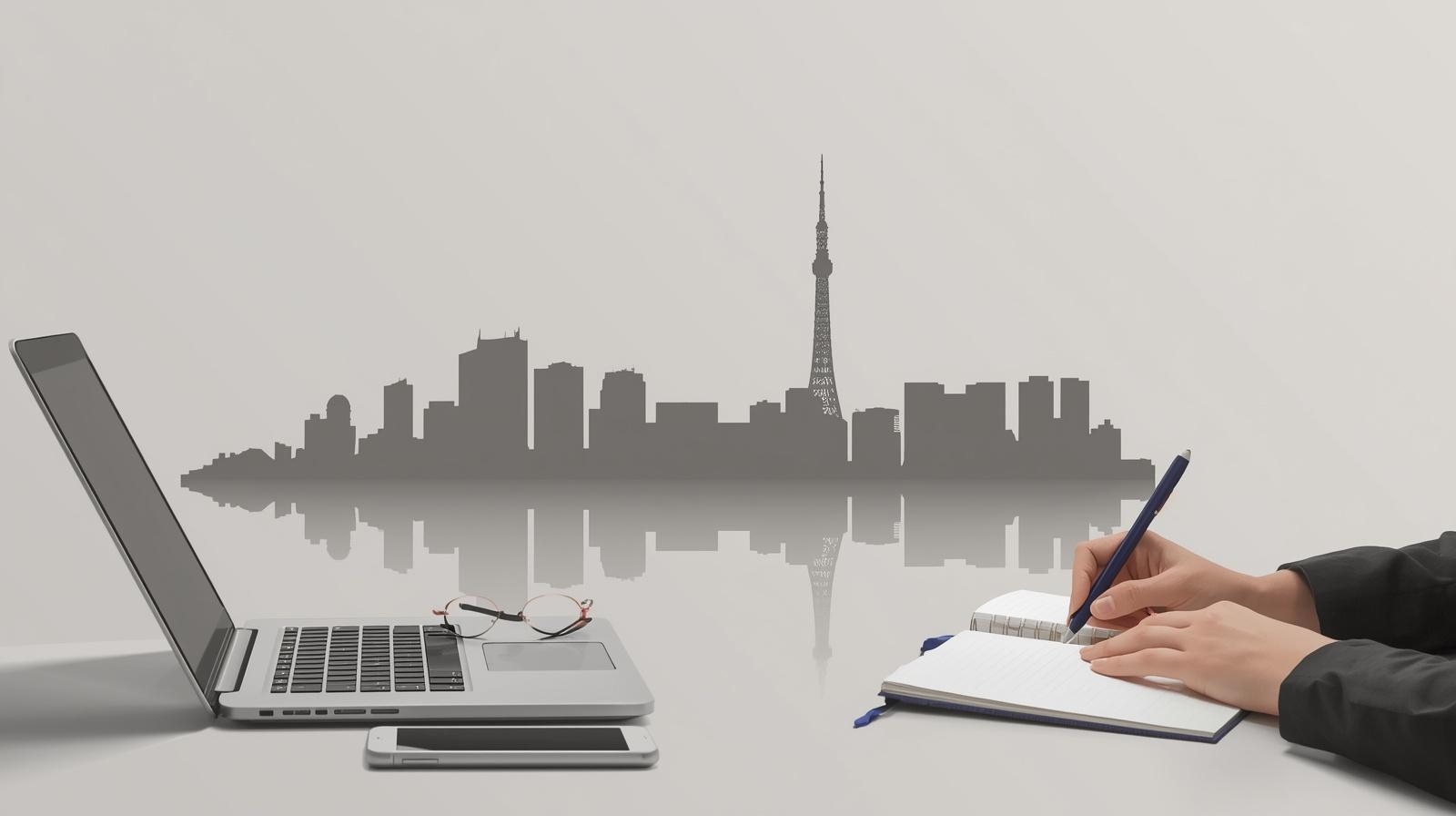 Laptop and notebook on a desk with a Tokyo skyline silhouette in the background, representing UX research and fieldwork in Japan.