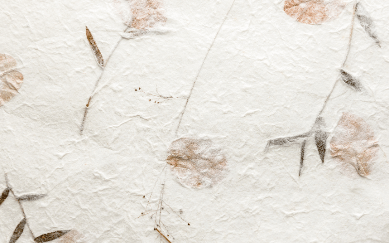A close-up shot of textured, handmade paper with dried flowers and leaves embedded within it. The image visually represents the importance of 'texture' when choosing stationery.