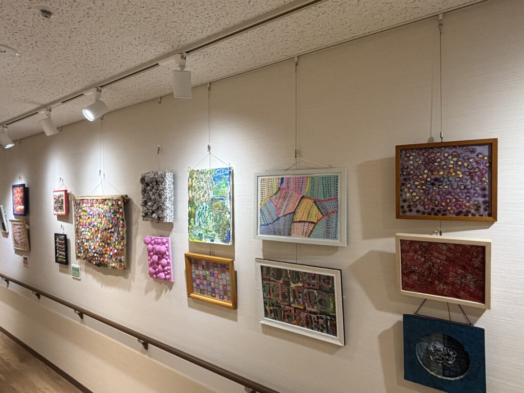 壁面に、布や紙、立体素材などを使った色鮮やかな作品が複数展示されている。